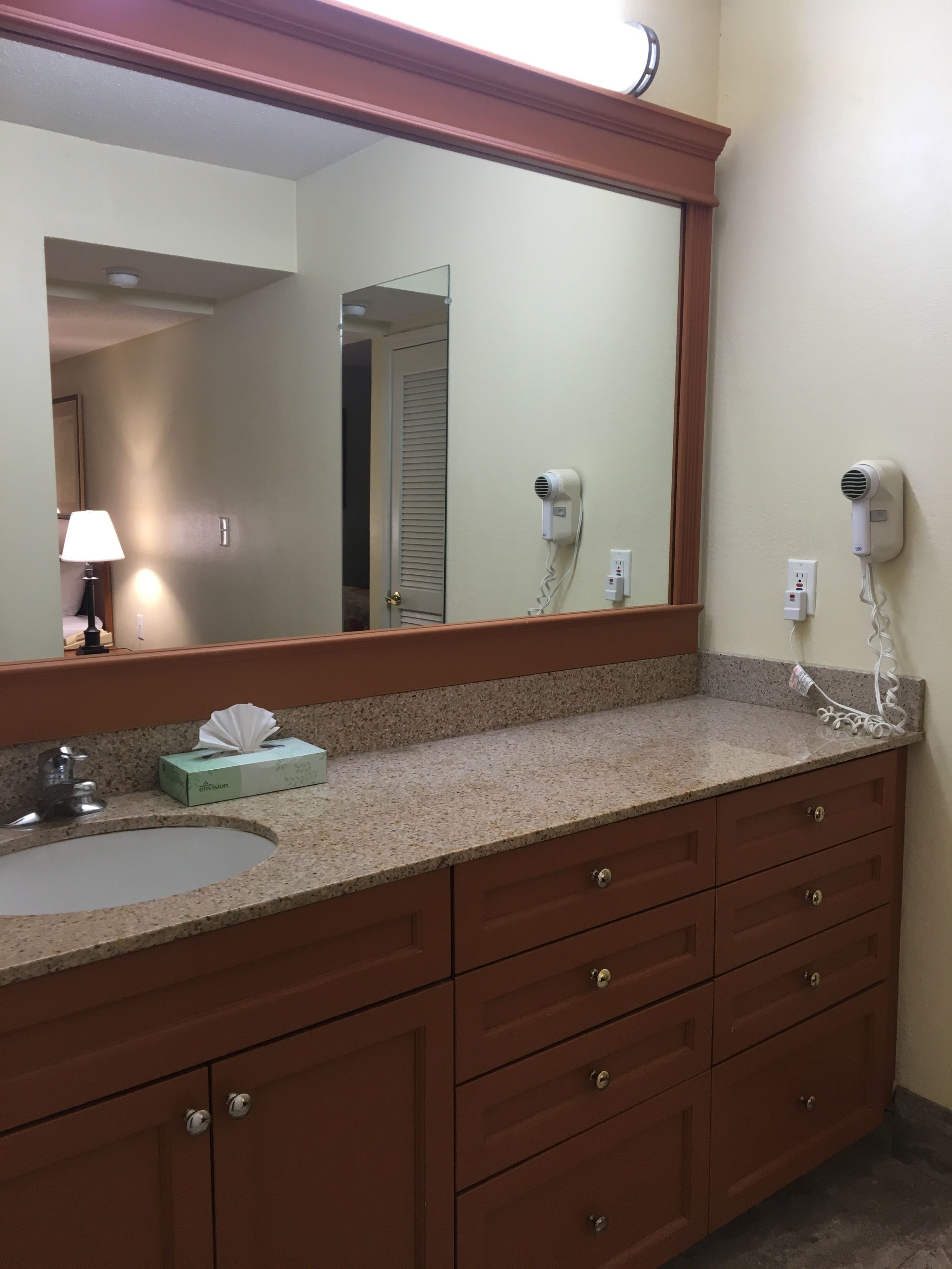 A bathroom with a granite countertop, a sink, a mirror, a hairdryer, and a tissue box.