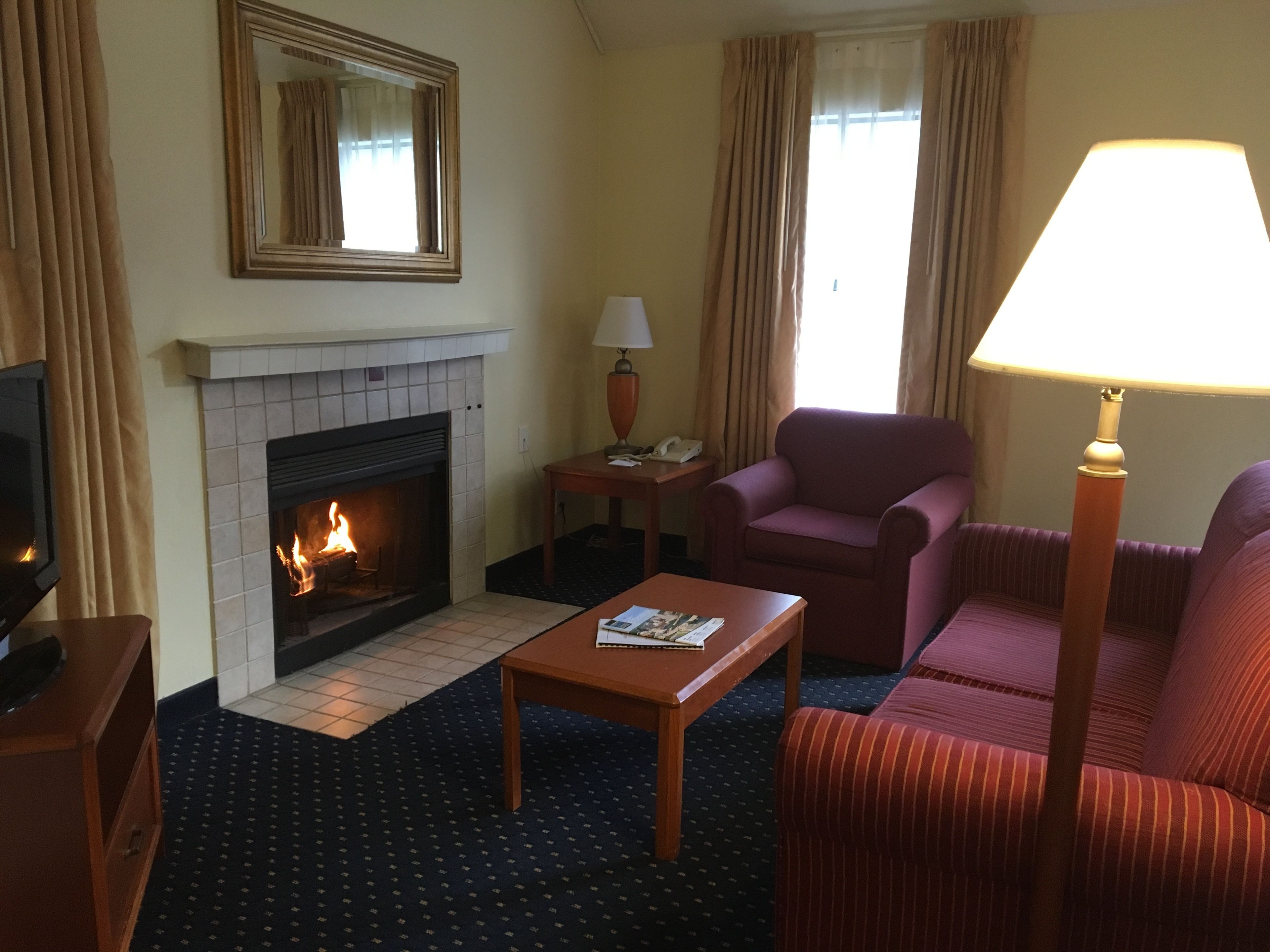 A hotel room with a fireplace, a television, a sofa, a table, and a lamp.