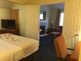 A hotel room with a bed, a TV, a fireplace, a chair, and a table.