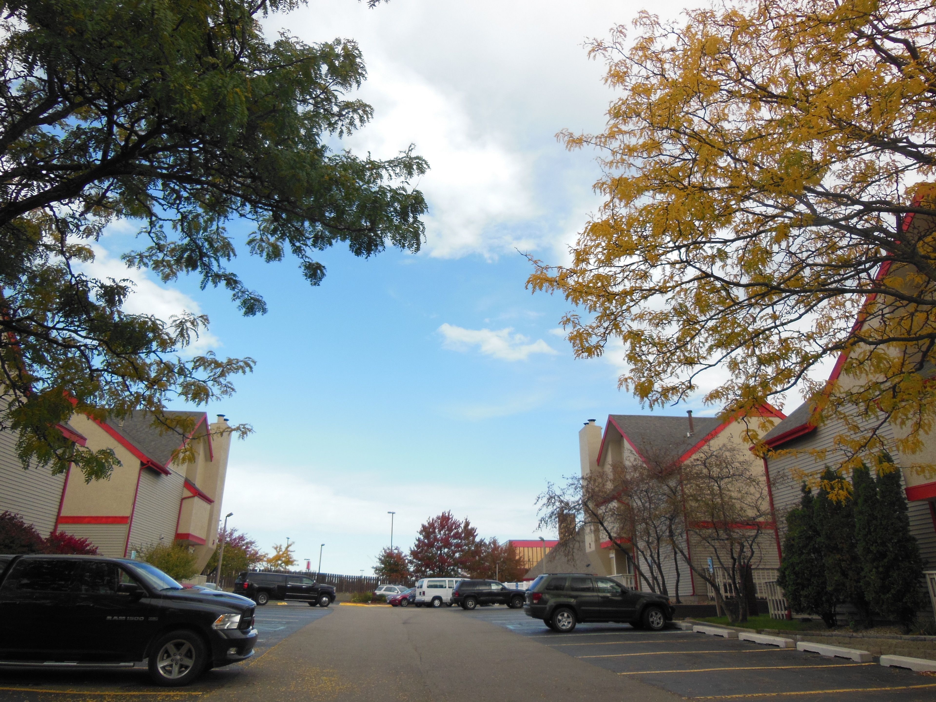 A parking lot with several cars, surrounded by buildings with red roofs and trees with yellow leaves.