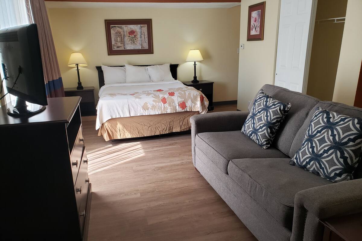 Une chambre d’hôtel comprenant un lit, un canapé, un bureau avec un ordinateur, deux lampes de chevet et un tableau au mur.