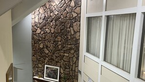 A living room with a stone wall, a fireplace, a framed picture, and a window with curtains. - Birch Hill Grand Rapids (Grand Rapids)