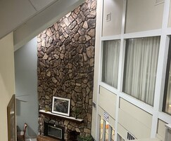 A living room with a stone wall, a fireplace, a framed picture, and a window with curtains.