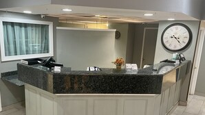 A reception area with a marble counter, a clock, and a television on the wall. - Birch Hill Grand Rapids (Grand Rapids)