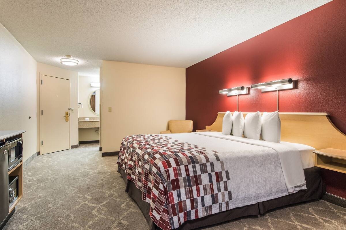A hotel room with a large bed, a desk, a microwave, and a red accent wall.