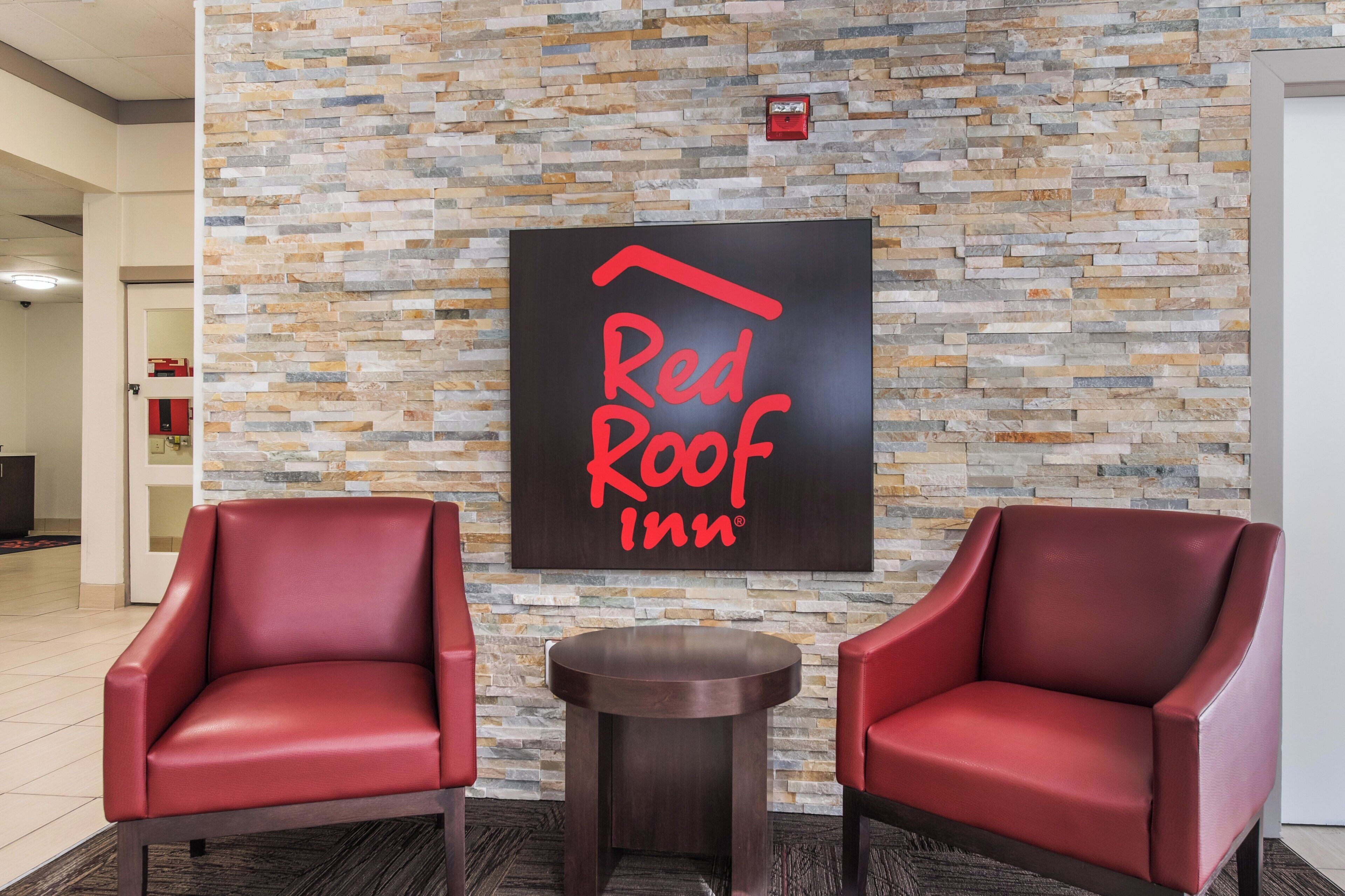 A Red Roof Inn lobby with a stone wall and two red leather chairs.