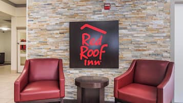 A Red Roof Inn lobby with a stone wall and two red leather chairs.