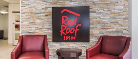 A Red Roof Inn lobby with a stone wall and two red leather chairs.
