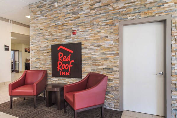 A Red Roof Inn lobby with a stone mosaic wall, two red armchairs, a small round table, and a door. - Red Roof Inn Seattle Airport - SEATAC (SeaTac)