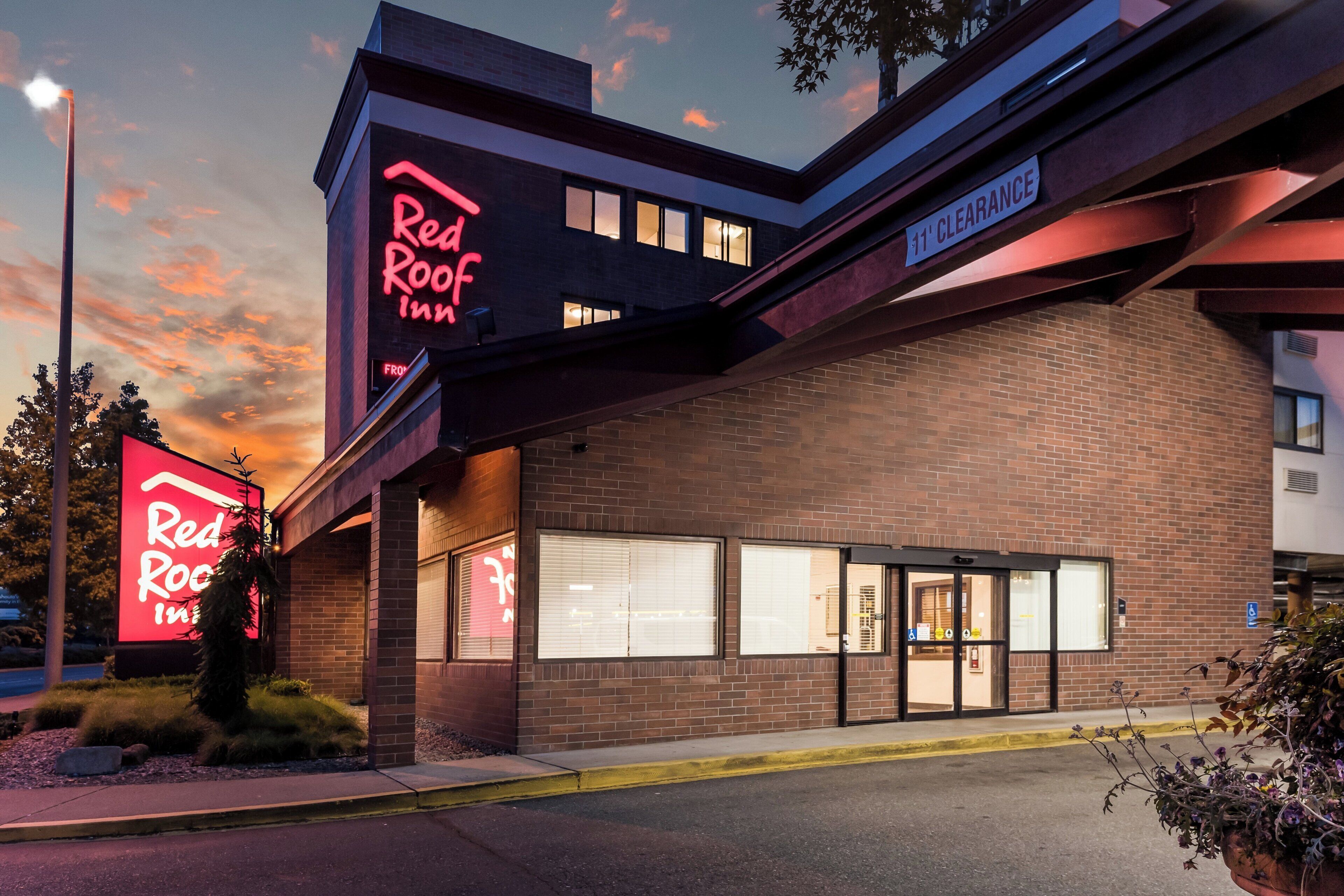A Red Roof Inn with a brick facade, large windows, and a clear sky in the background.
