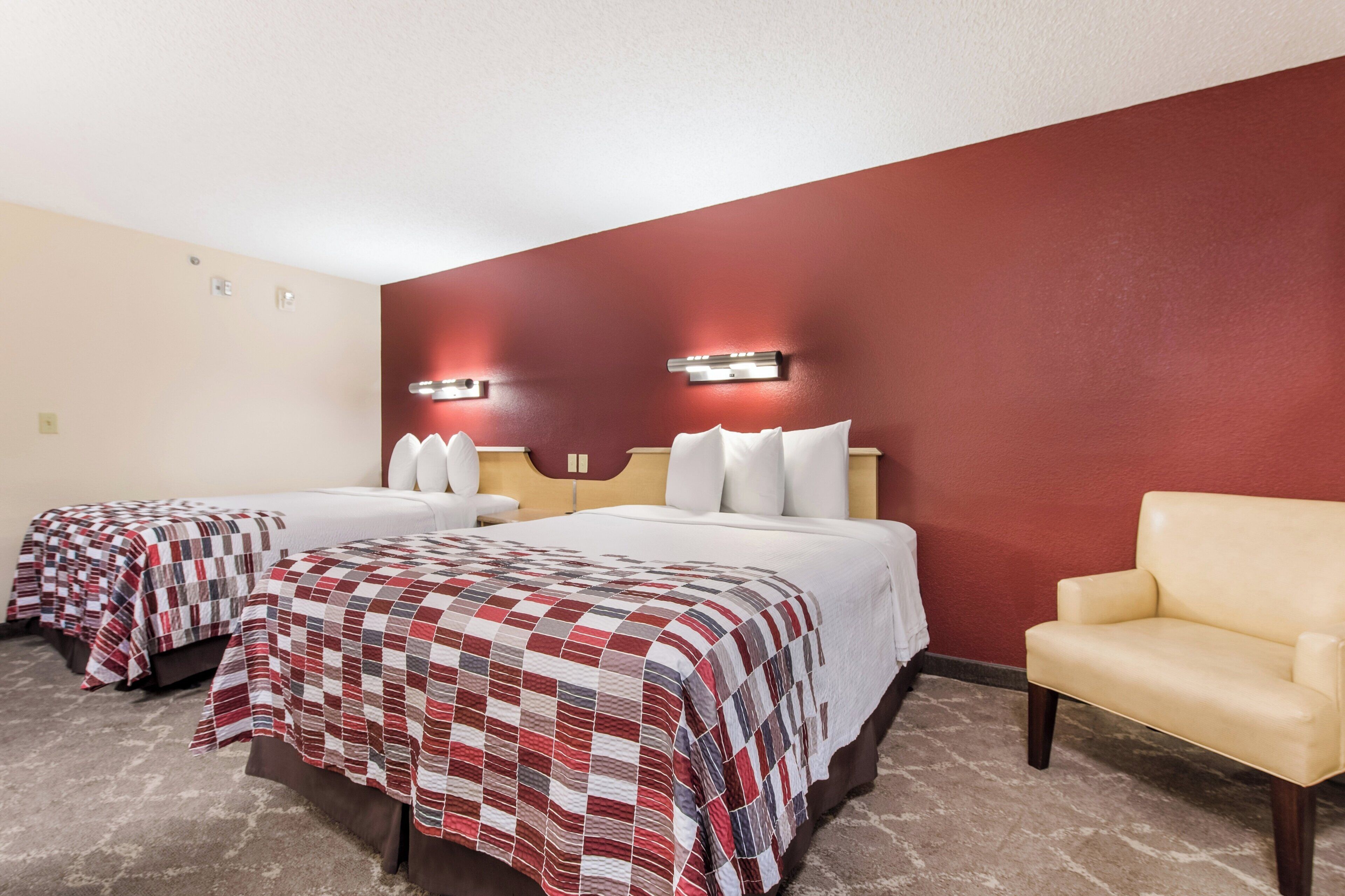 Habitación de hotel con dos camas, una silla y una pared de acento roja.