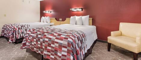 Habitación de hotel con dos camas, una silla y una pared de acento roja.