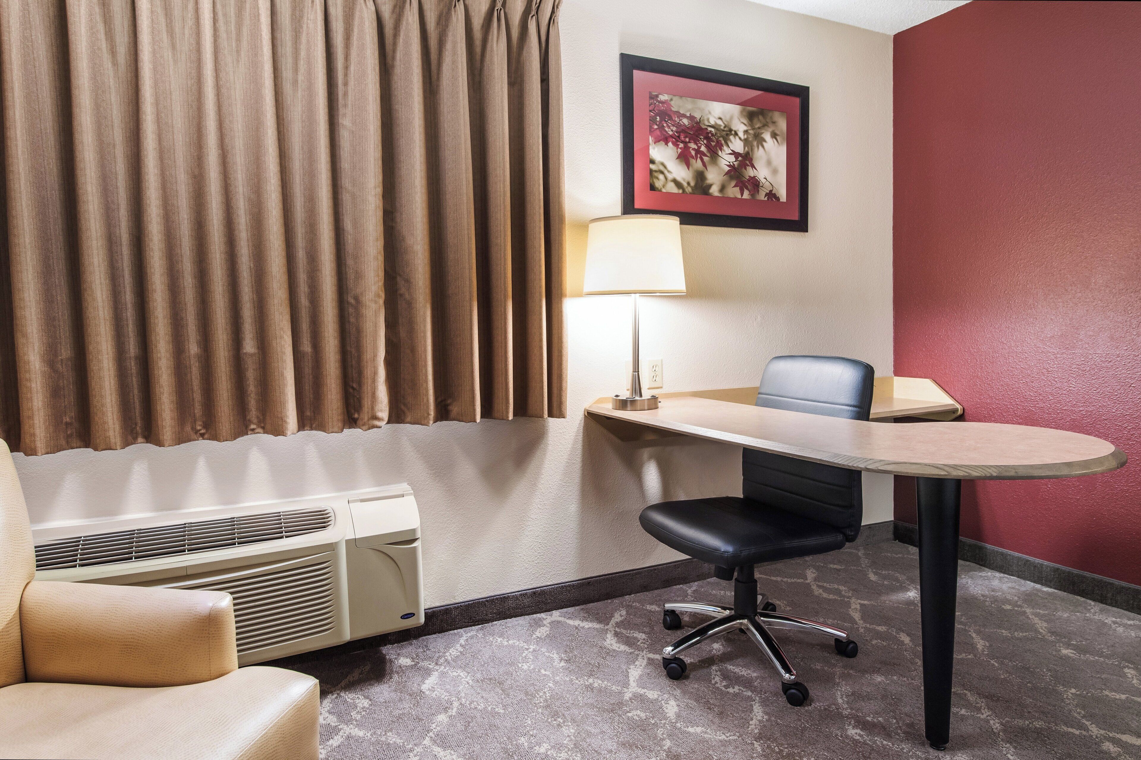 A hotel room with a bed, a desk with a chair, a lamp, and a heater.