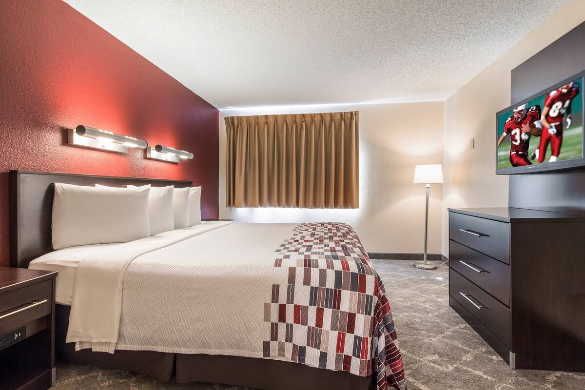 A hotel room with a large bed, a desk, a dresser, a TV, and a window with curtains.