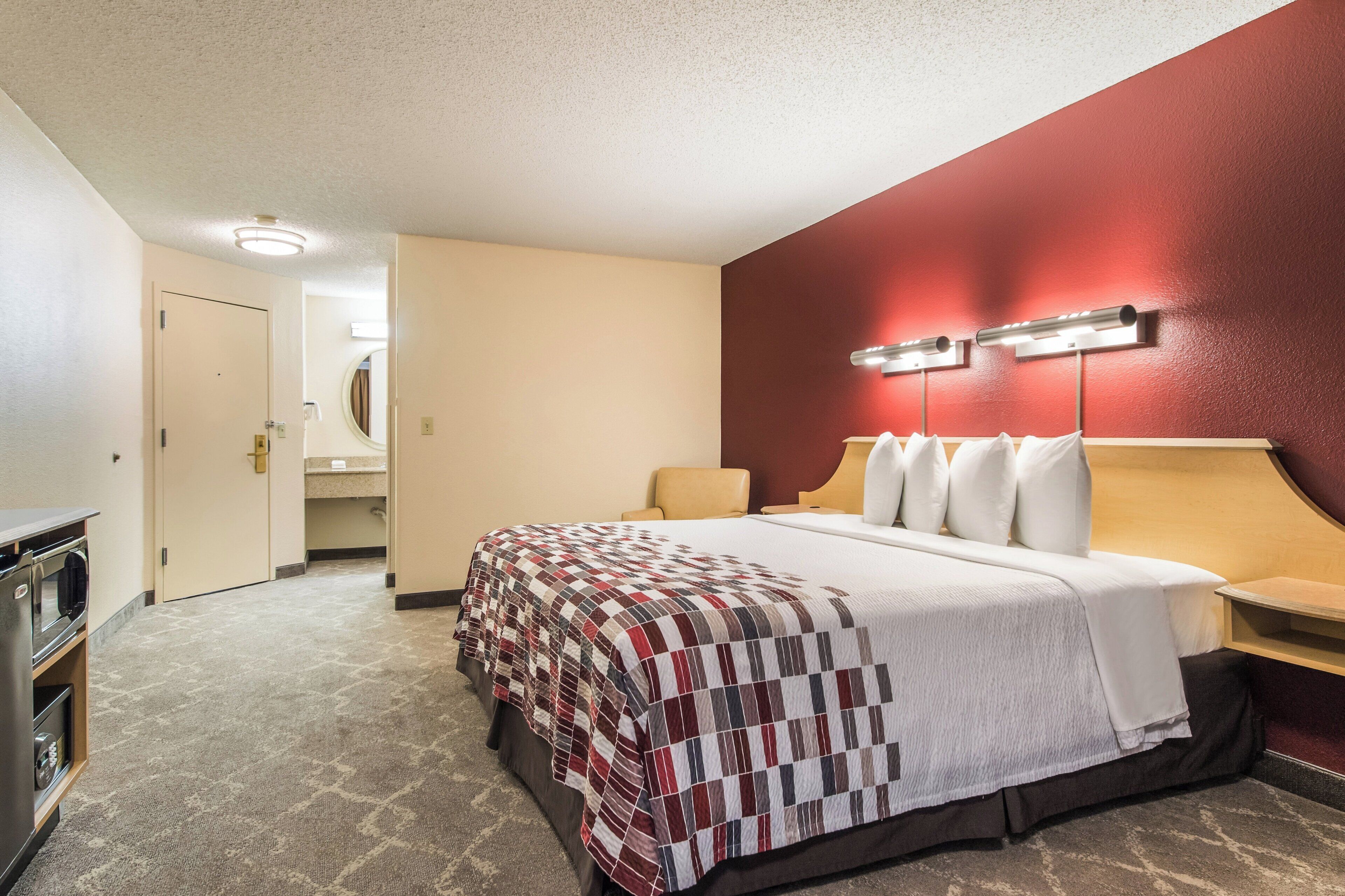 A hotel room with a bed, a nightstand, a lamp, a mirror, and a door leading to a bathroom.
