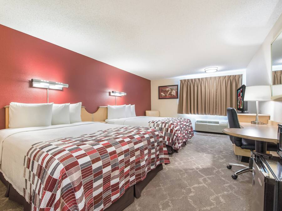 Habitación de hotel con dos camas, un escritorio, una silla, un televisor y un espejo.