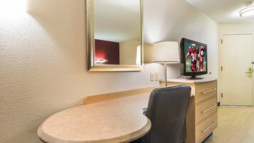 A hotel room with a round table, a chair, a television on a dresser, a mirror, and a lamp.