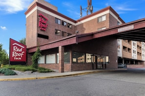 Un Red Roof Inn con fachada de ladrillo, un acceso cubierto y un estacionamiento en el fondo.