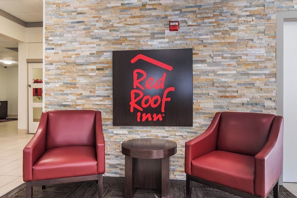 Um saguão do Red Roof Inn com uma parede de pedra, duas poltronas de couro vermelho e uma mesa redonda pequena.