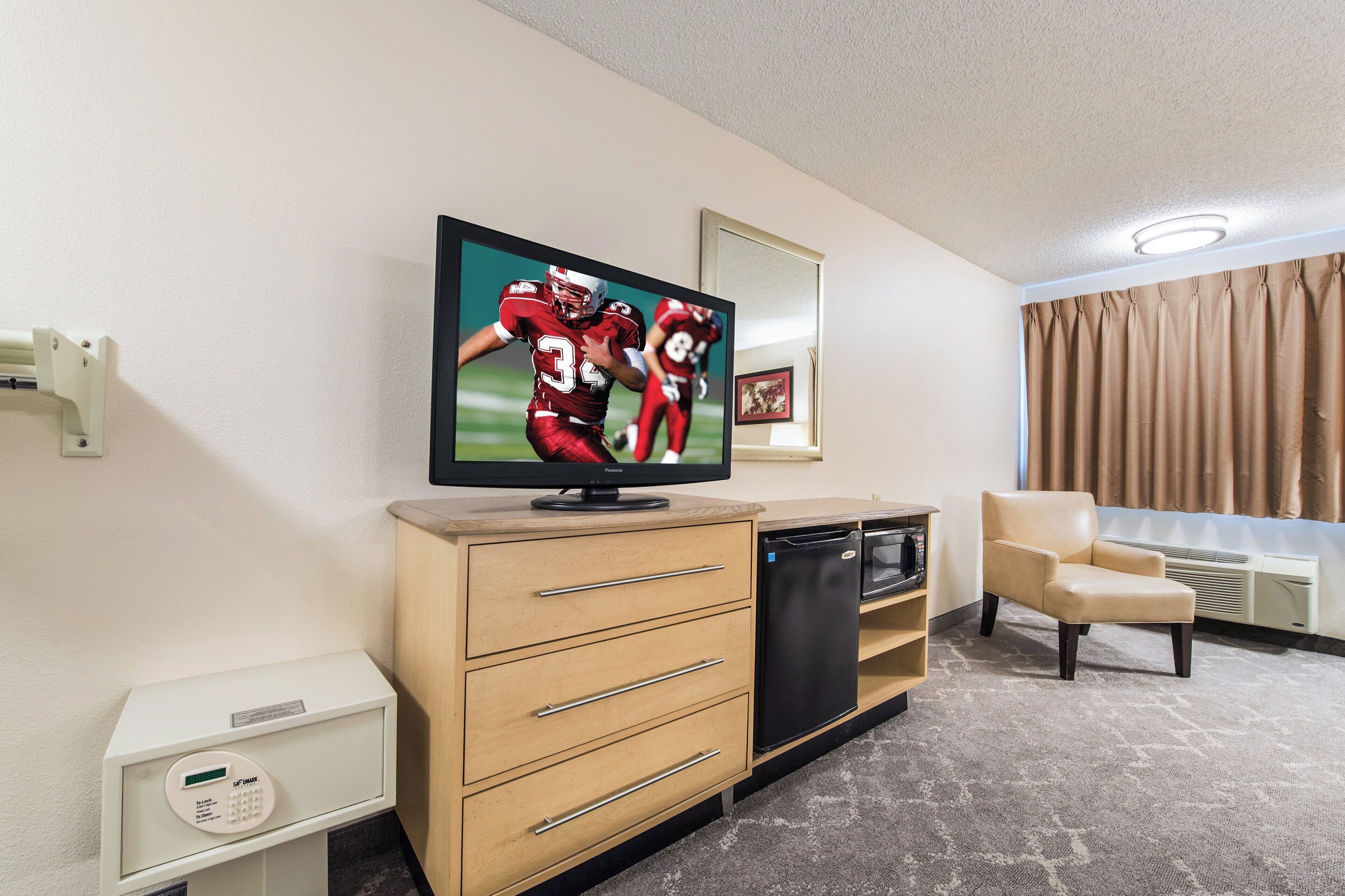 A hotel room with a television, a sofa, a desk, and a minibar.