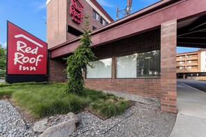Ein Red Roof Inn mit auffälliger Beschilderung, einer Ziegel-Fassade und einem kleinen Baum davor.