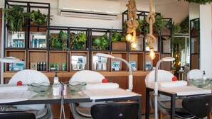 Un salón con mostrador de recepción, sillas, estanterías con plantas y una lámpara colgante.