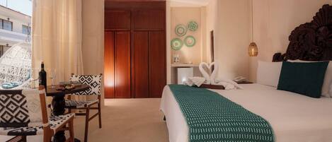 A hotel room with a bed, a desk with chairs, a minibar, and a view of the outside.