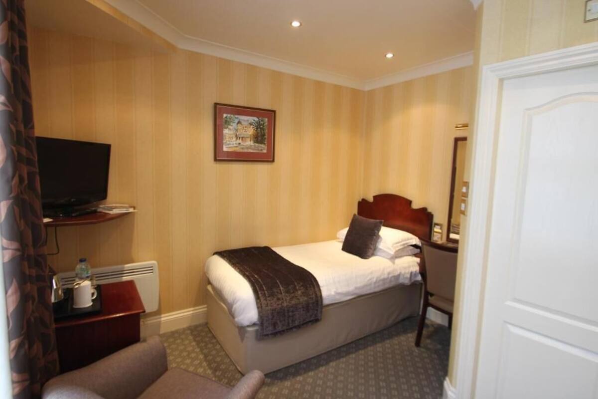Une chambre d’hôtel comprenant un lit, une télévision, un bureau avec une chaise et un tableau encadré au mur.