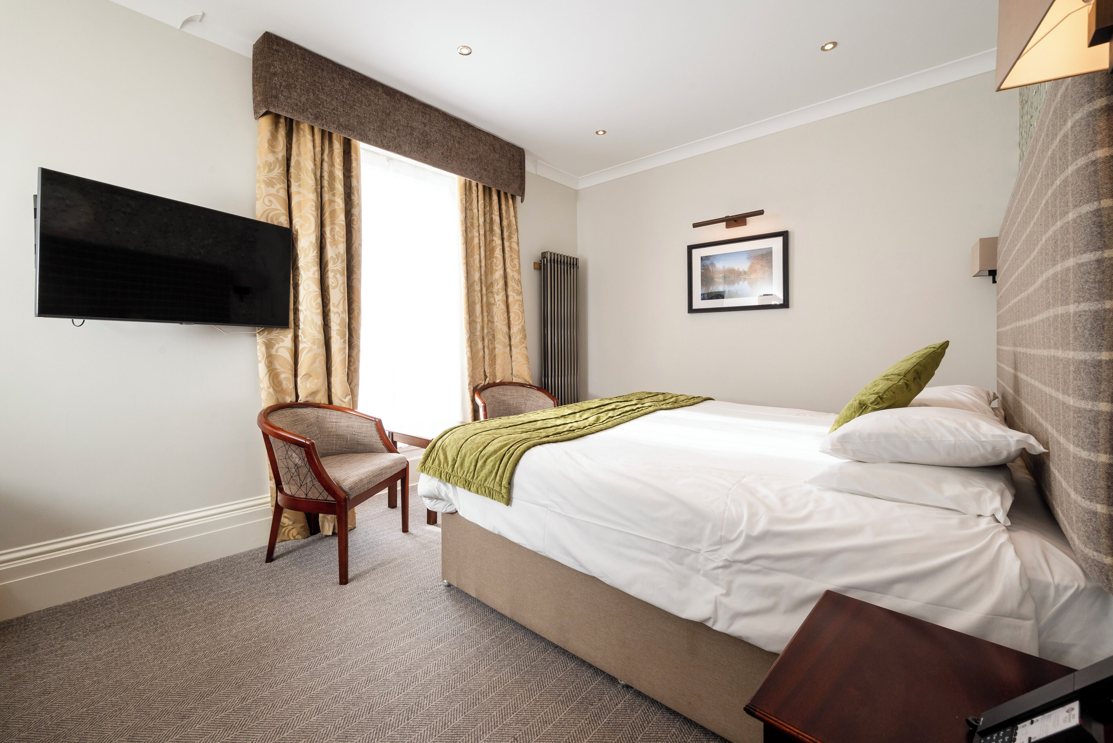 A hotel room with a bed, a chair, a television, and a picture on the wall.