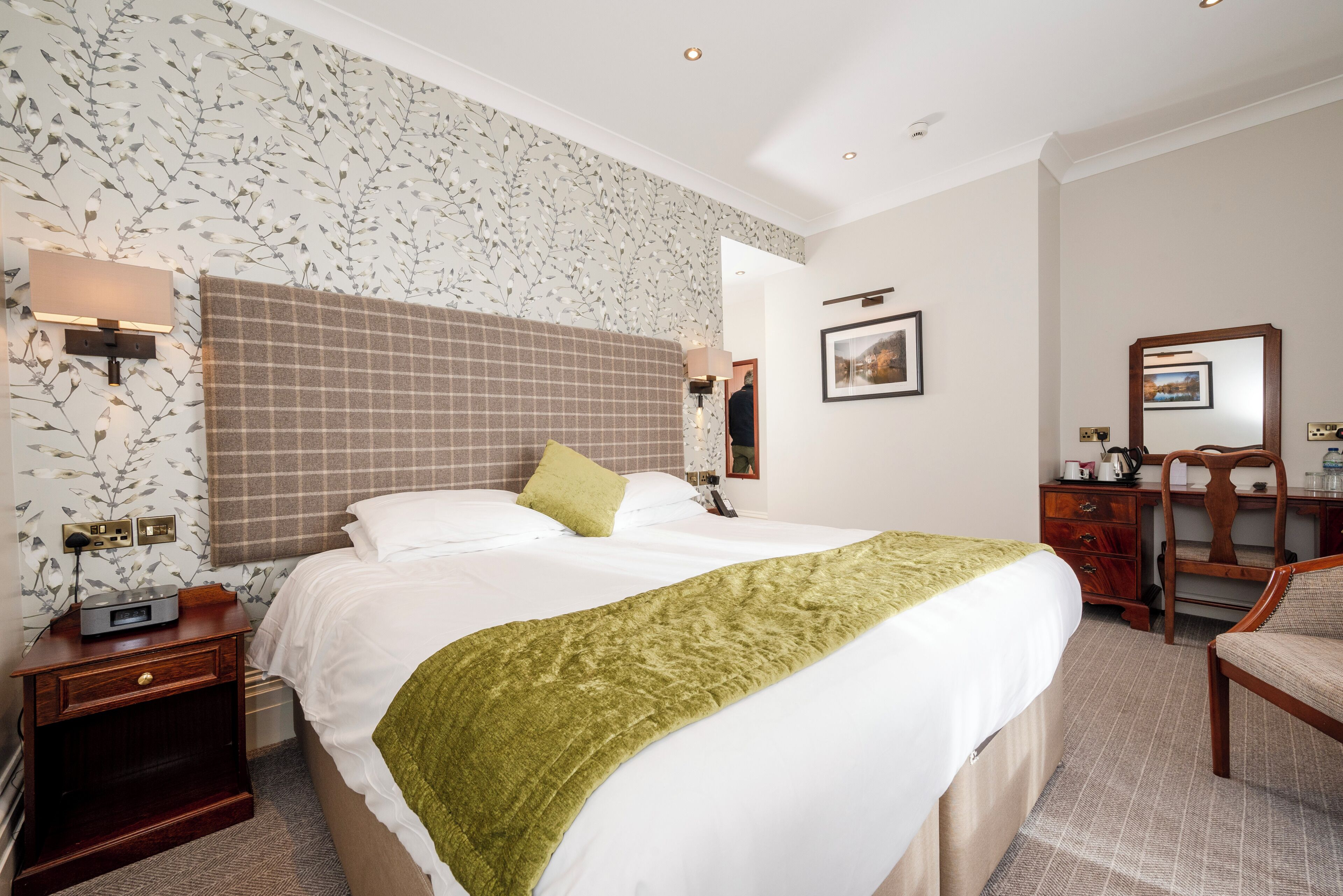 Habitación de hotel con una cama grande, una mesita de noche, un escritorio, una silla y una pared con estampado floral.