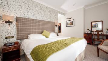 Habitación de hotel con una cama grande, una mesita de noche, un escritorio, una silla y una pared con estampado floral.