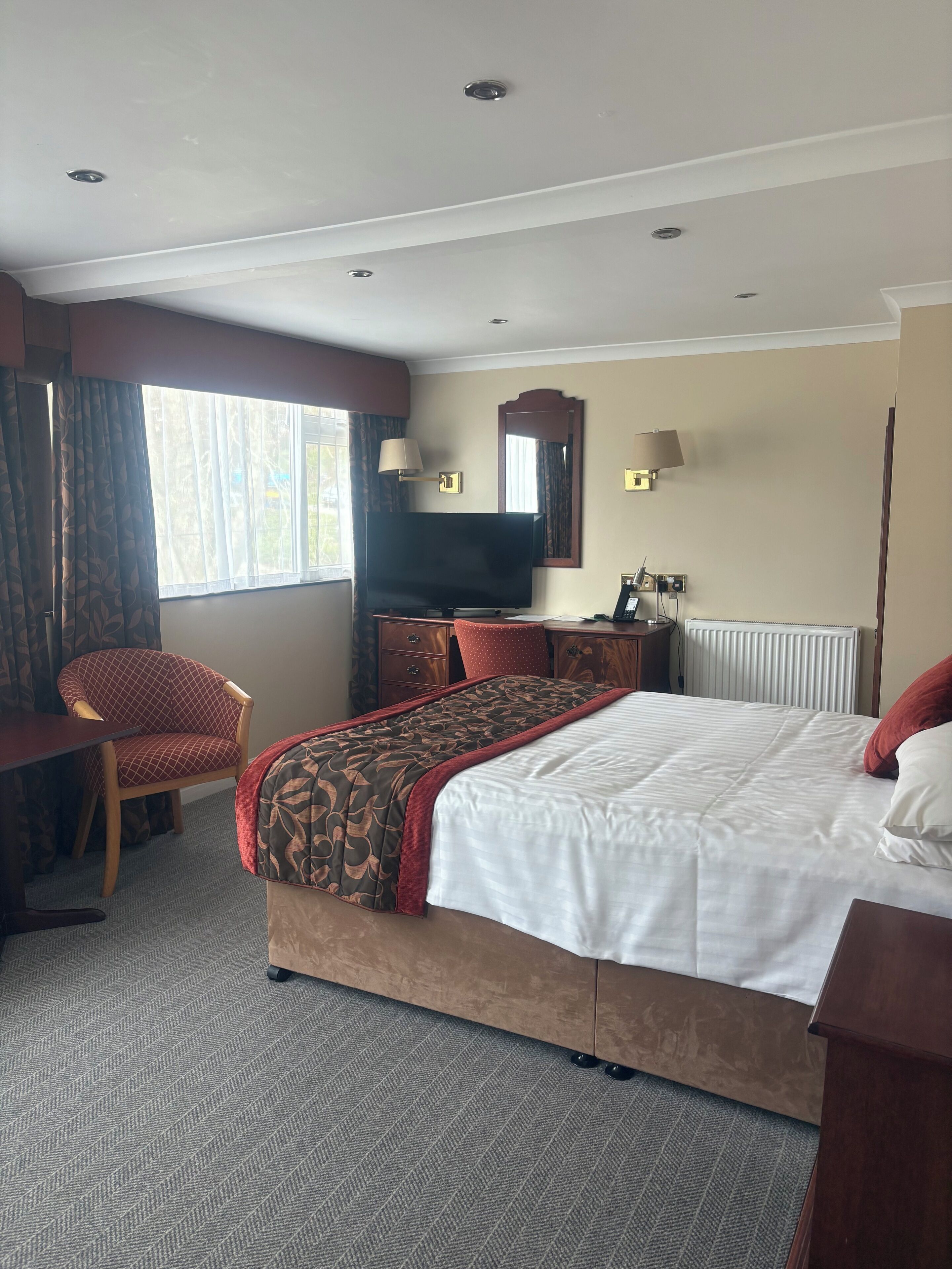 Une chambre d’hôtel avec un lit, un bureau, une chaise, une télévision, un miroir et une fenêtre.