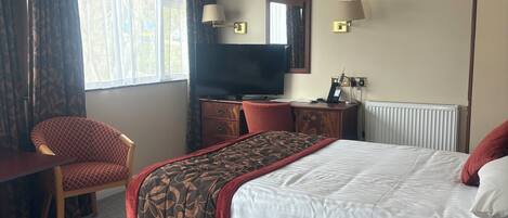 Une chambre d’hôtel avec un lit, un bureau, une chaise, une télévision, un miroir et une fenêtre.