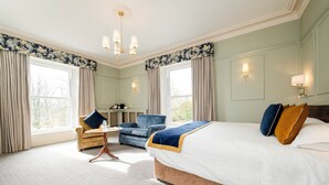 A hotel room with a large bed, two armchairs, a small table, and a chandelier.