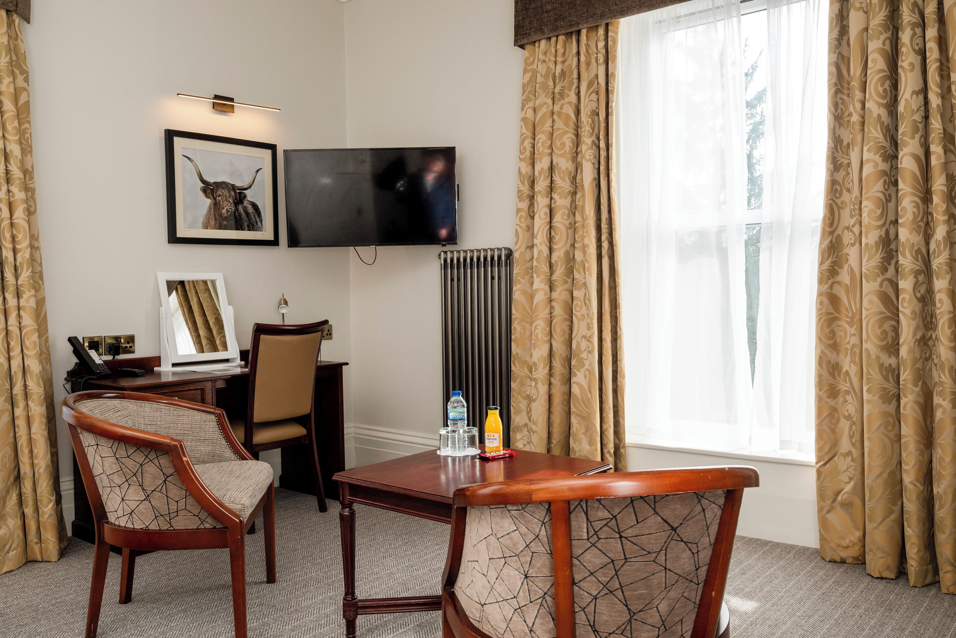 A hotel room with a desk, two chairs, a television, a framed picture, and a window with curtains.