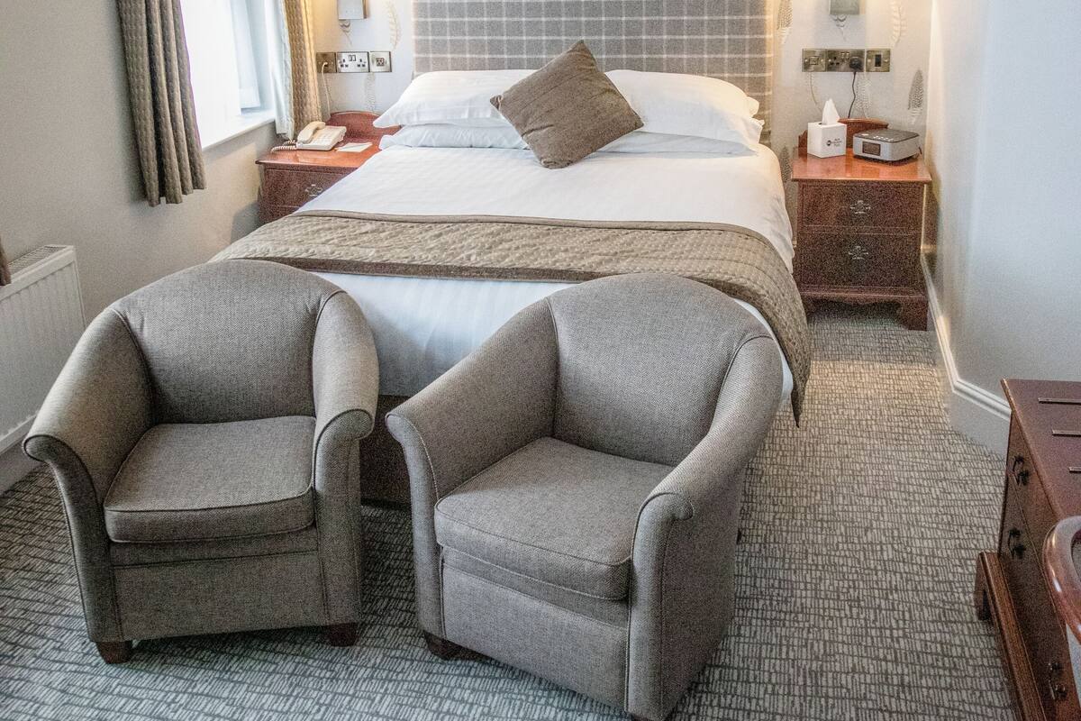 Une chambre d’hôtel avec un grand lit, deux tables de chevet avec des lampes, une chaise, une petite table et un tapis à motifs.