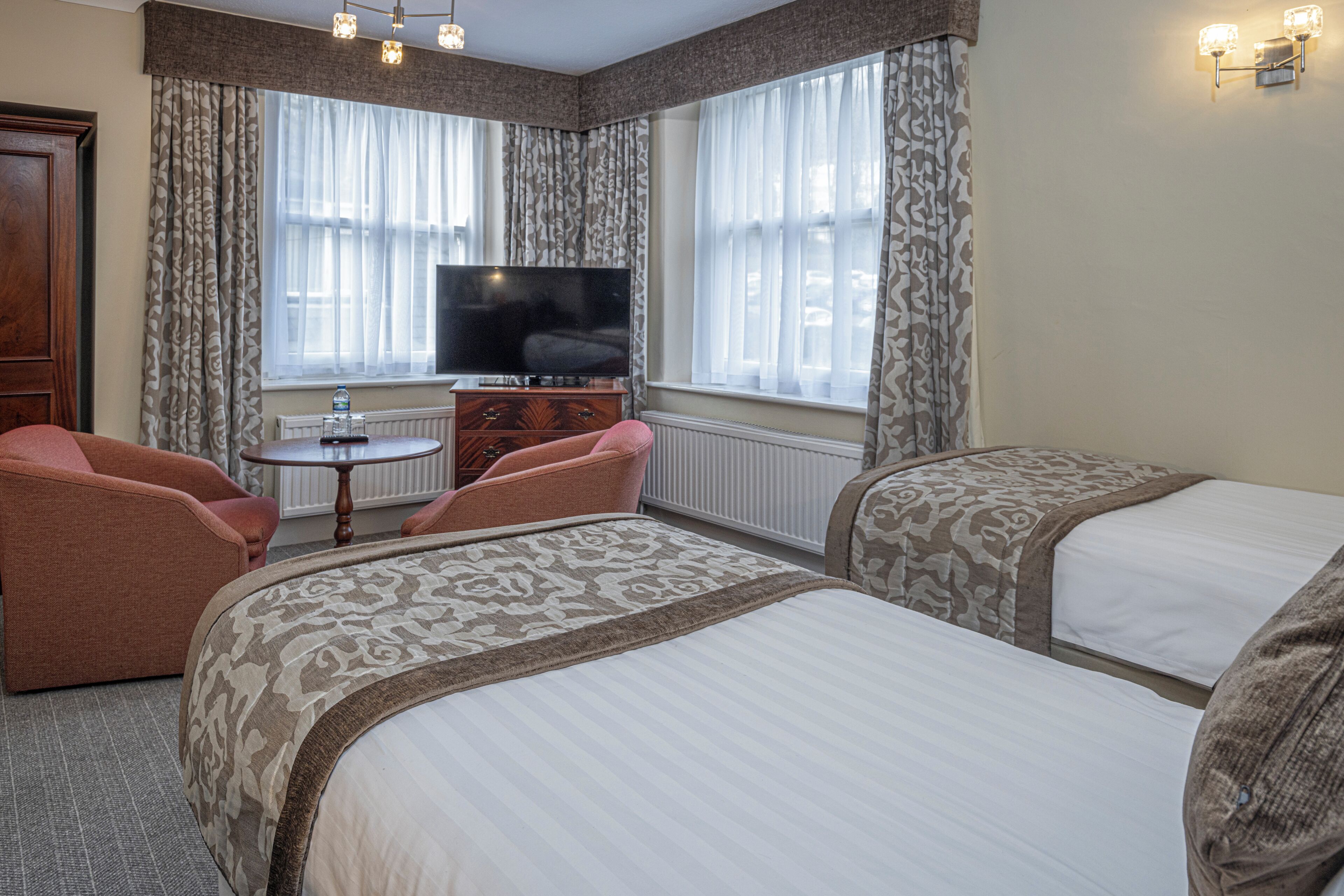 A hotel room with two beds, a television, a small table, and a chair.