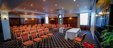A conference room with rows of orange chairs, a white table, and a patterned carpet.