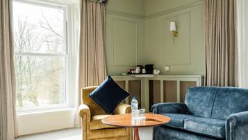 A room with a large window, a round wooden table, a blue sofa, and a gold-armored armchair.