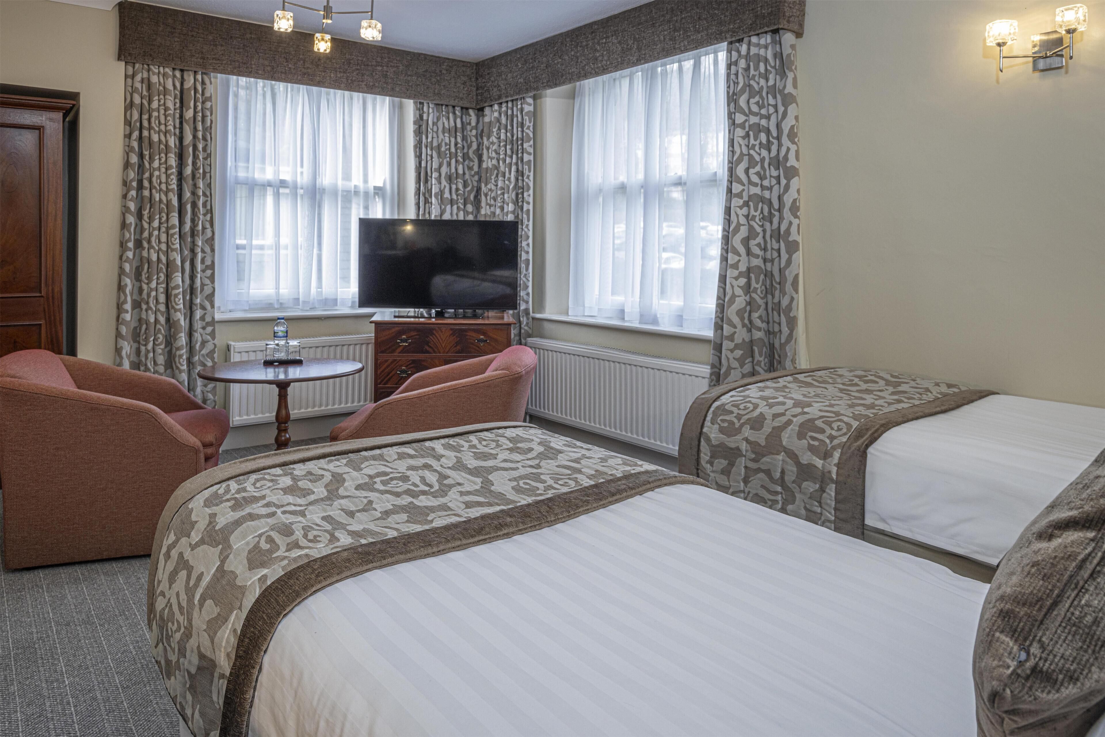 A hotel room with two beds, a television, a small table, and a chair.