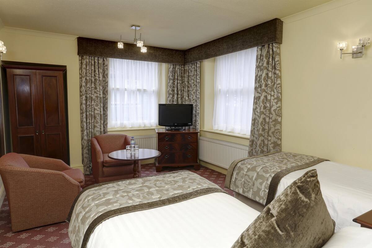 Une chambre d’hôtel avec deux lits, une télévision, une armoire en bois, une chaise et une petite table.