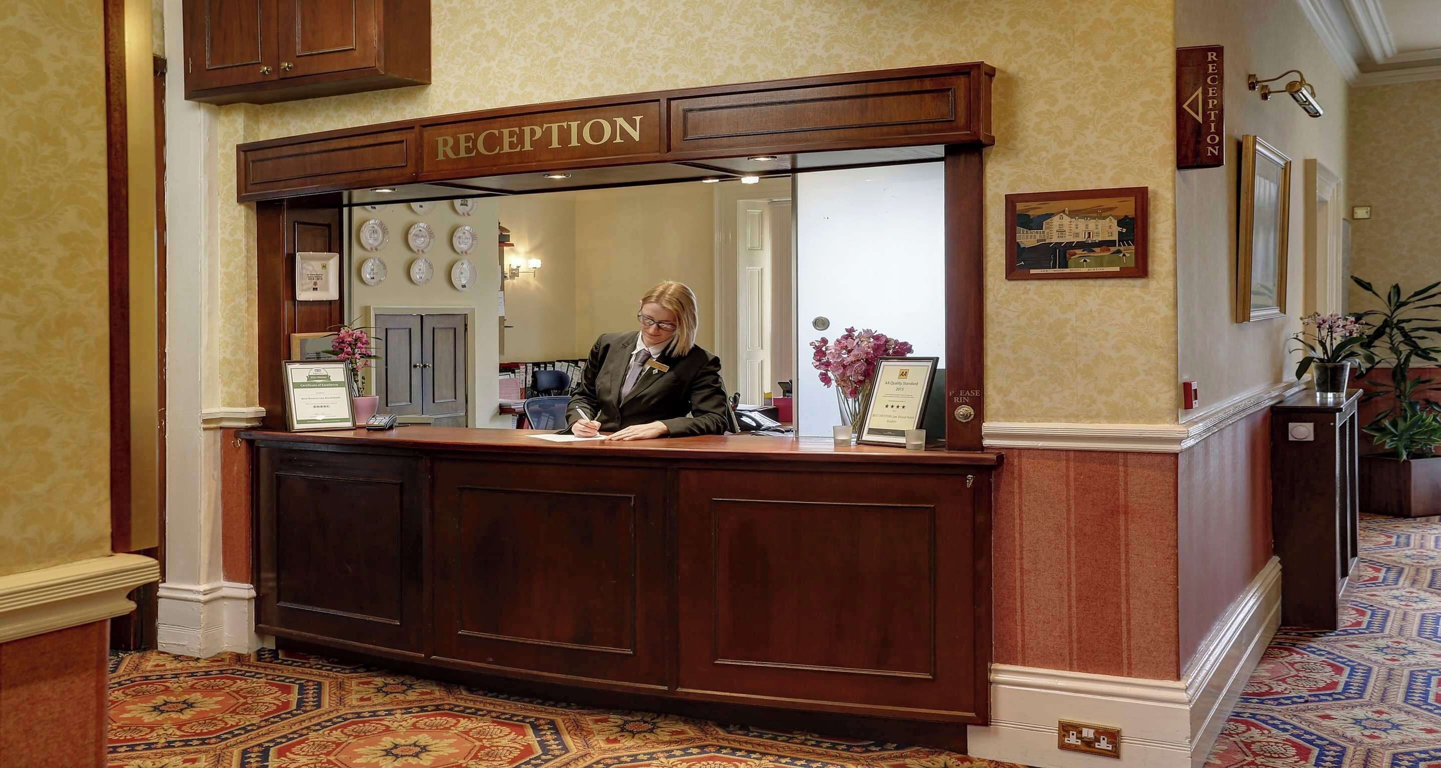 A reception desk with a 'RECEPTION' sign above it, a framed certificate, and a potted plant to the right.