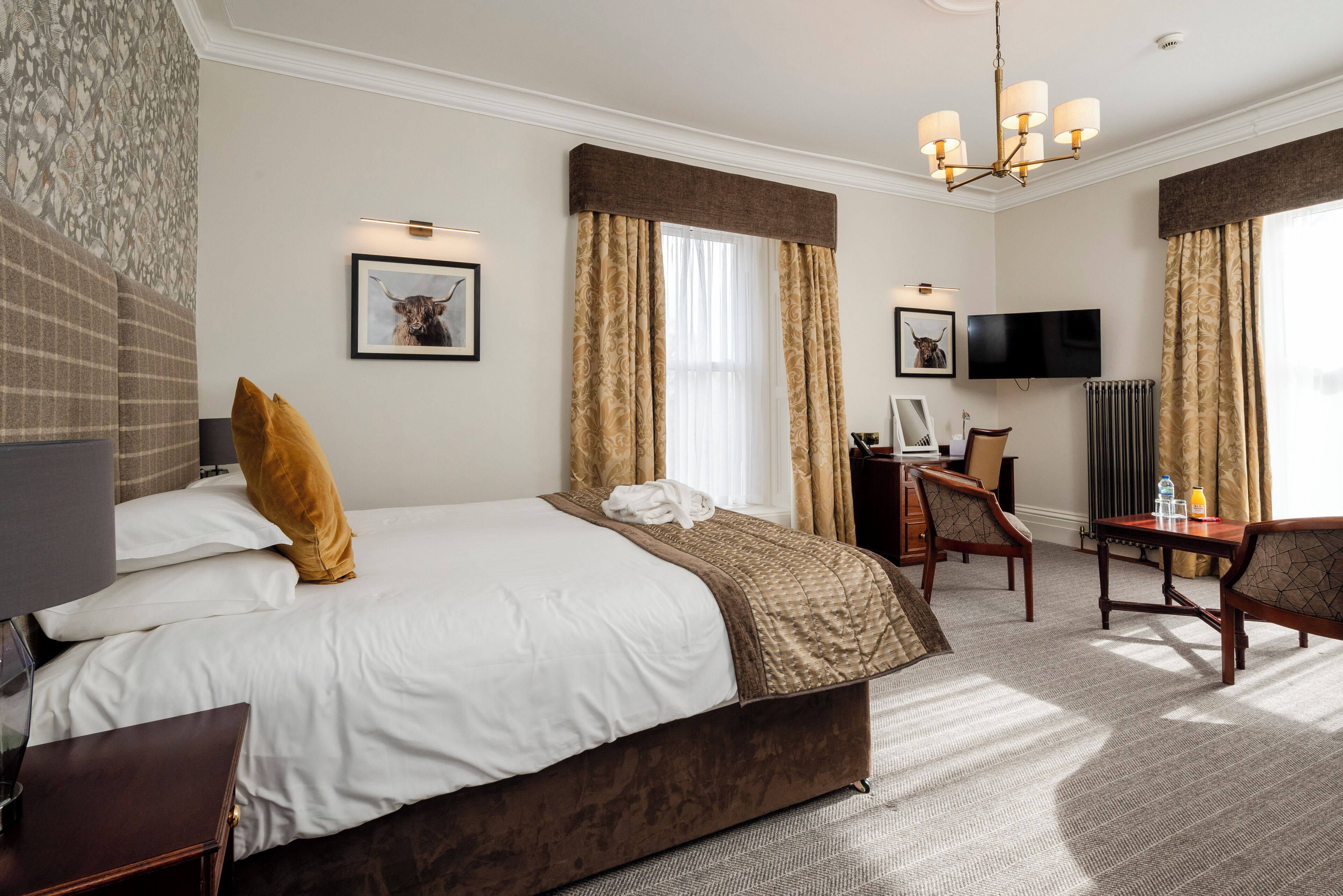 A hotel room with a large bed, a desk, a chair, a television, and a chandelier.