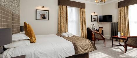 A hotel room with a large bed, a desk, a chair, a television, and a chandelier.