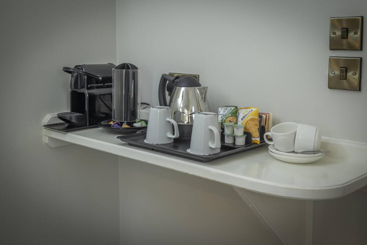 Un comptoir pour le petit-déjeuner équipé d’une machine à café, d’une bouilloire et d’un plateau avec des tasses et une boîte de céréales.