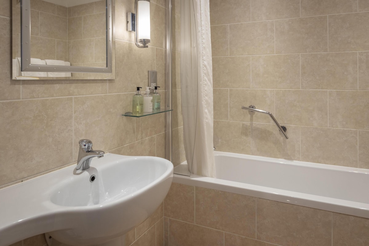 A bathroom with a sink, mirror, shower, and tiled walls.