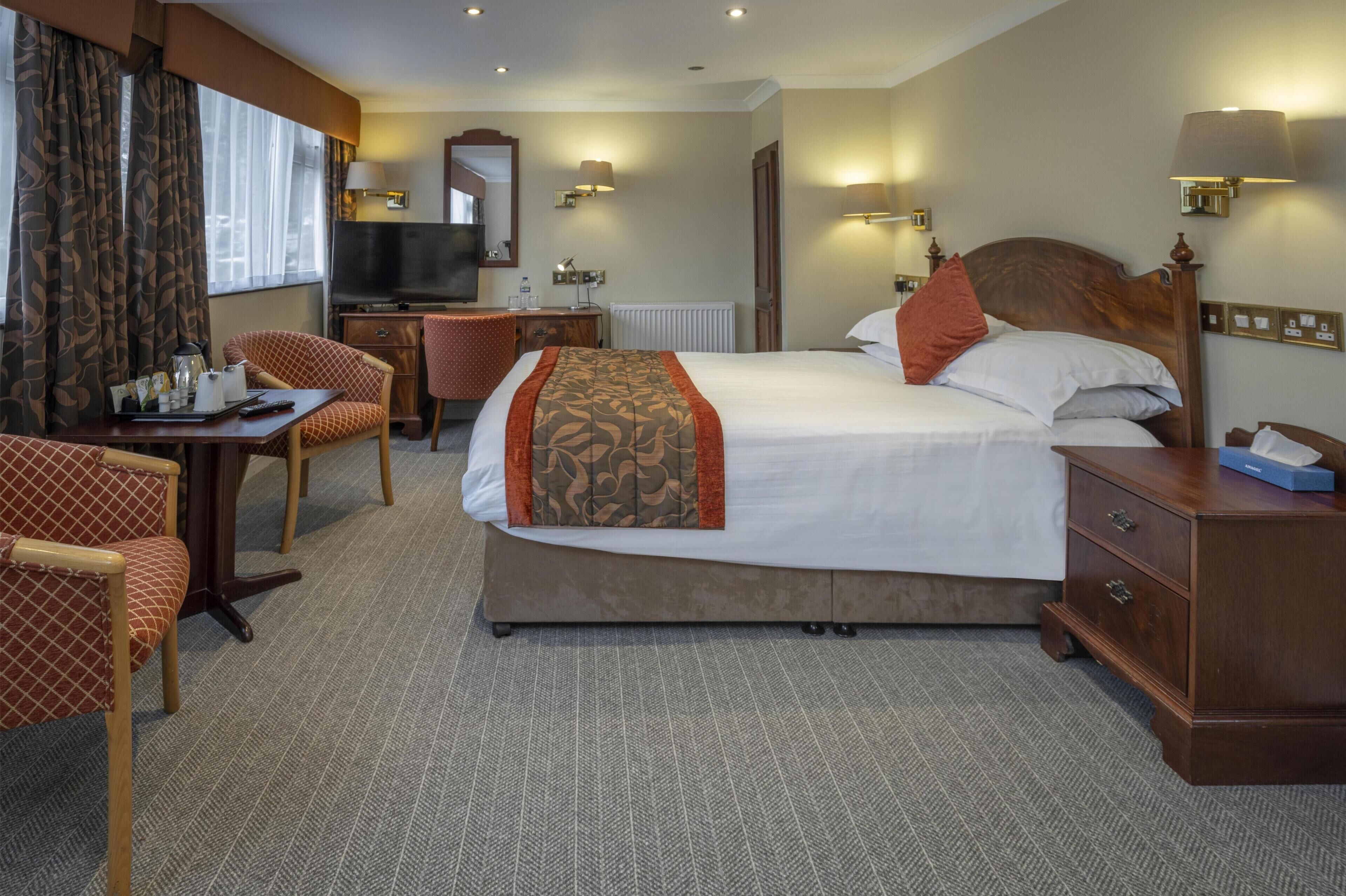 A hotel room with a bed, a desk, a chair, a television, and a dresser.