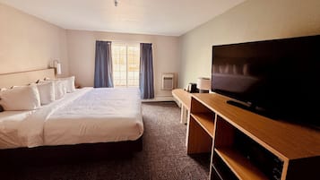 A hotel room with a large bed, a flat-screen TV on a wooden stand, a desk, and a window with curtains.