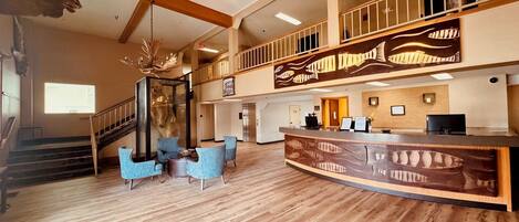 A spacious lobby with a wooden floor, a reception desk, and a staircase leading to an upper level.