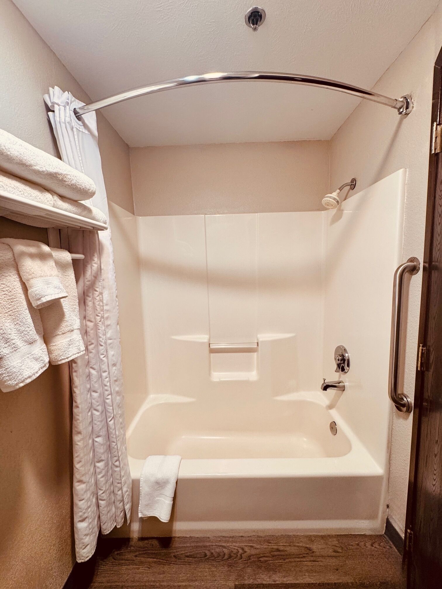 A walk-in shower with a glass door, a towel rack with folded towels, and a wooden floor.